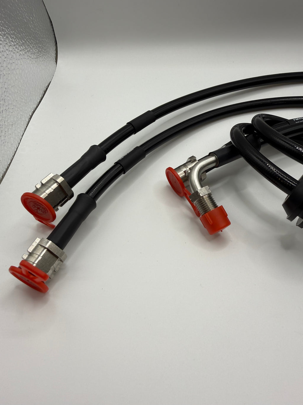 Black performance valve controller hoses with metal connectors and red caps on white background