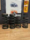 Four heavy-duty valve springs with retainers on a wooden table, automotive art in background, Eastwood Engineering UK performance parts.