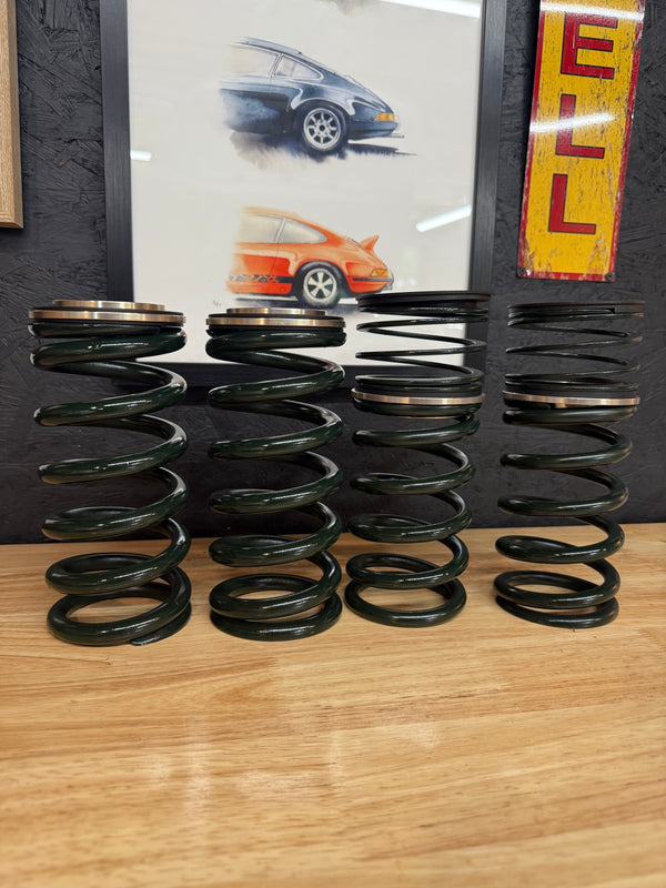 Four heavy-duty valve springs with retainers on a wooden table, automotive art in background, Eastwood Engineering UK performance parts.