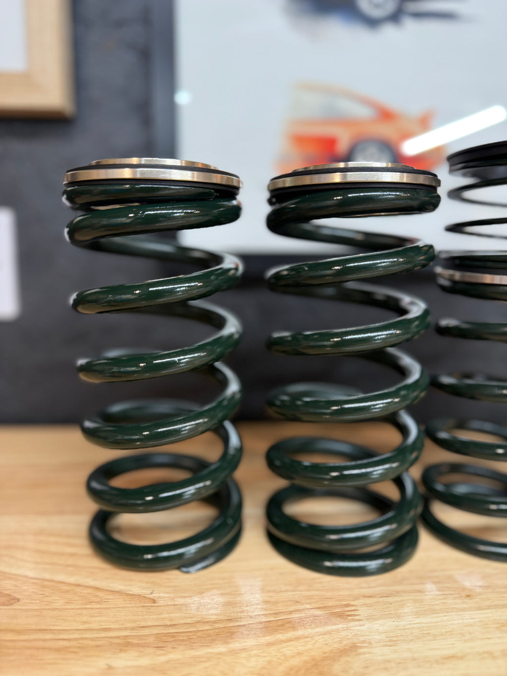 Pair of green automotive valve springs with metal caps on wooden surface, Eastwood Engineering